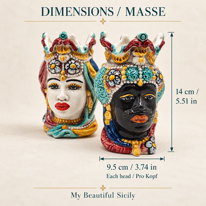 Two hand-painted Sicilian Moorish heads displayed on a stone console against a teal wall.