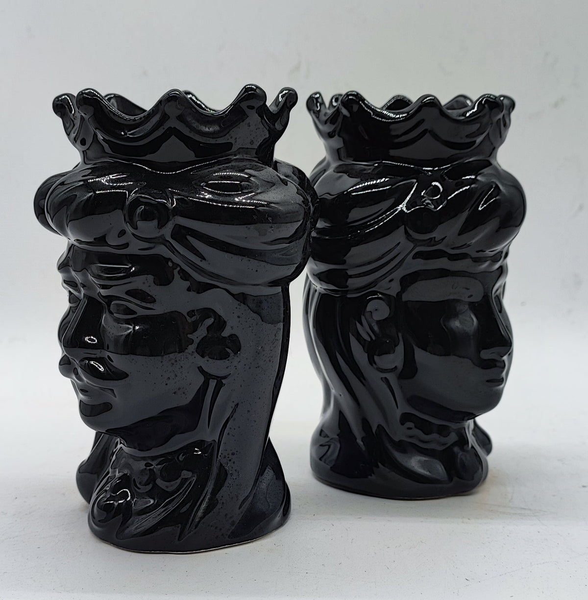 Side profile of two handmade black Sicilian Moorish Head ceramics showing sculpted crowns, facial details and glossy glaze.