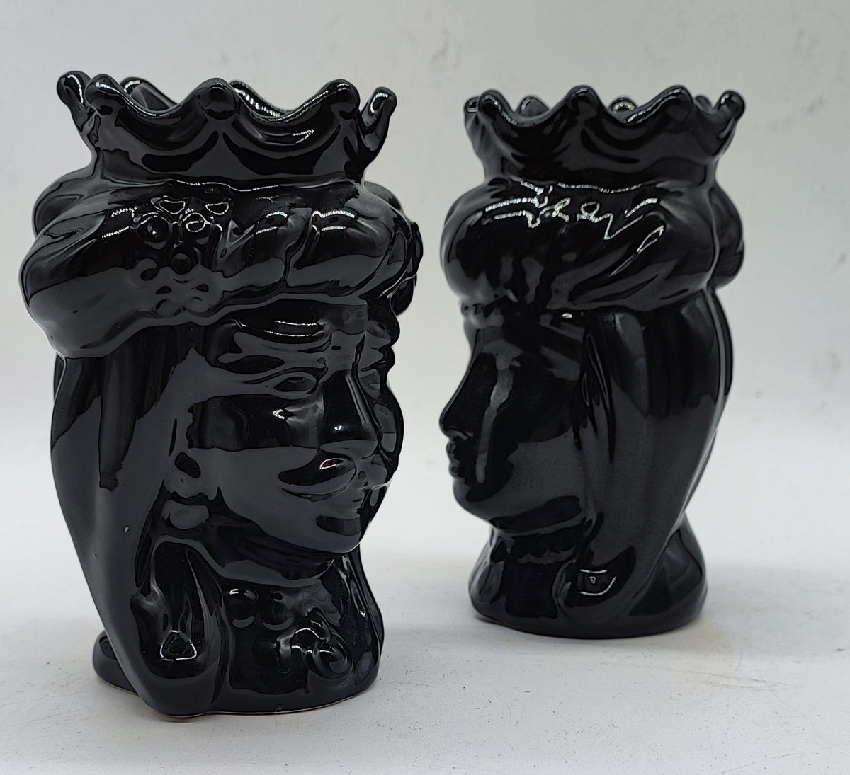 Side profile of two handmade black Sicilian Moorish Head ceramics showing sculpted crowns, facial details and glossy glaze.