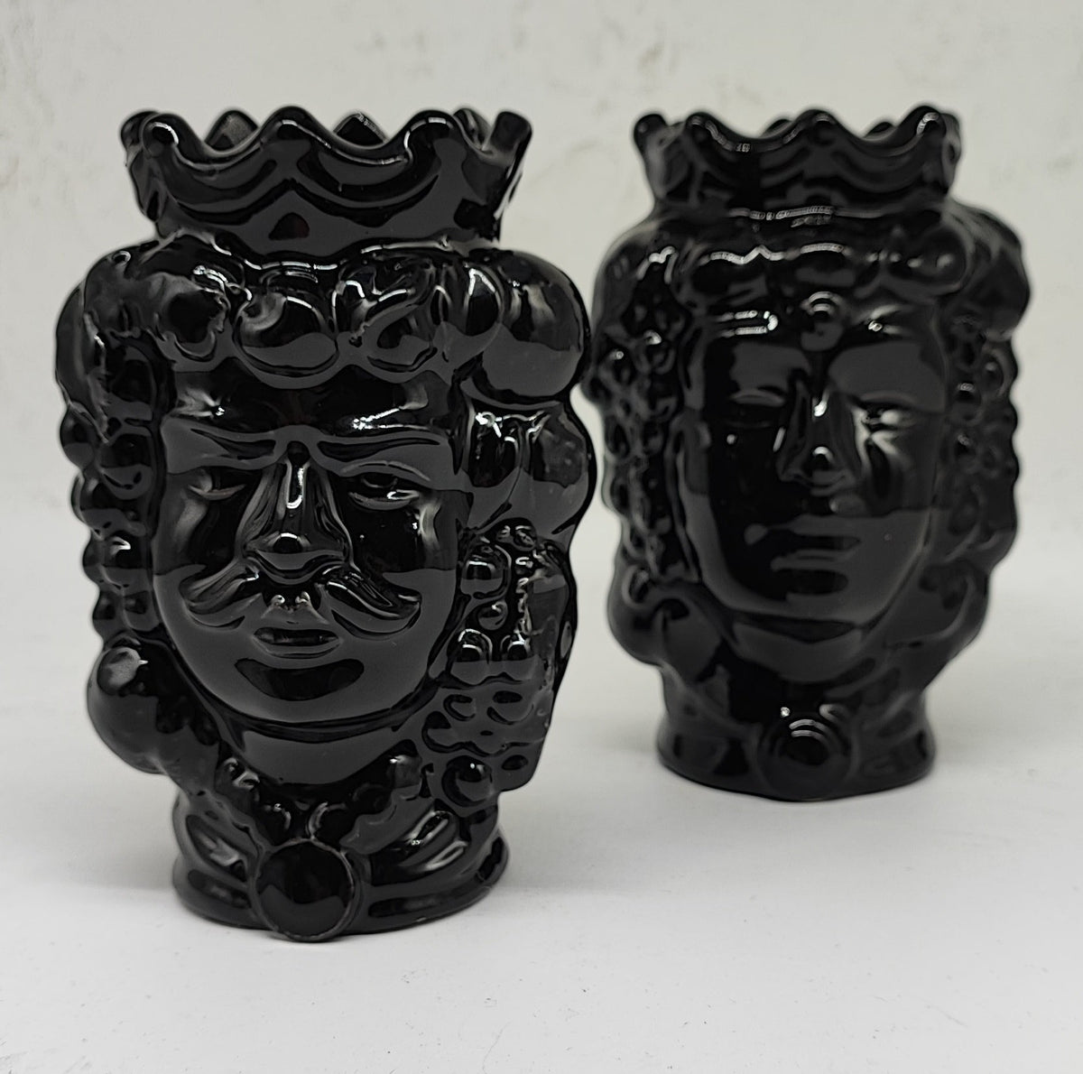 Two glossy black Sicilian Moorish head vases on a stone terrace with lemons and a sea view