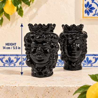 Two glossy black Sicilian ceramic Moorish heads, 14 cm tall, displayed on a stone terrace with lemons and a sea view.