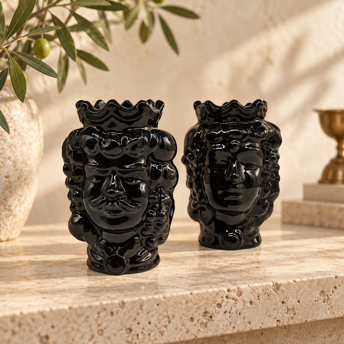 Two glossy black Sicilian Moorish head vases on a stone terrace with lemons and a sea view