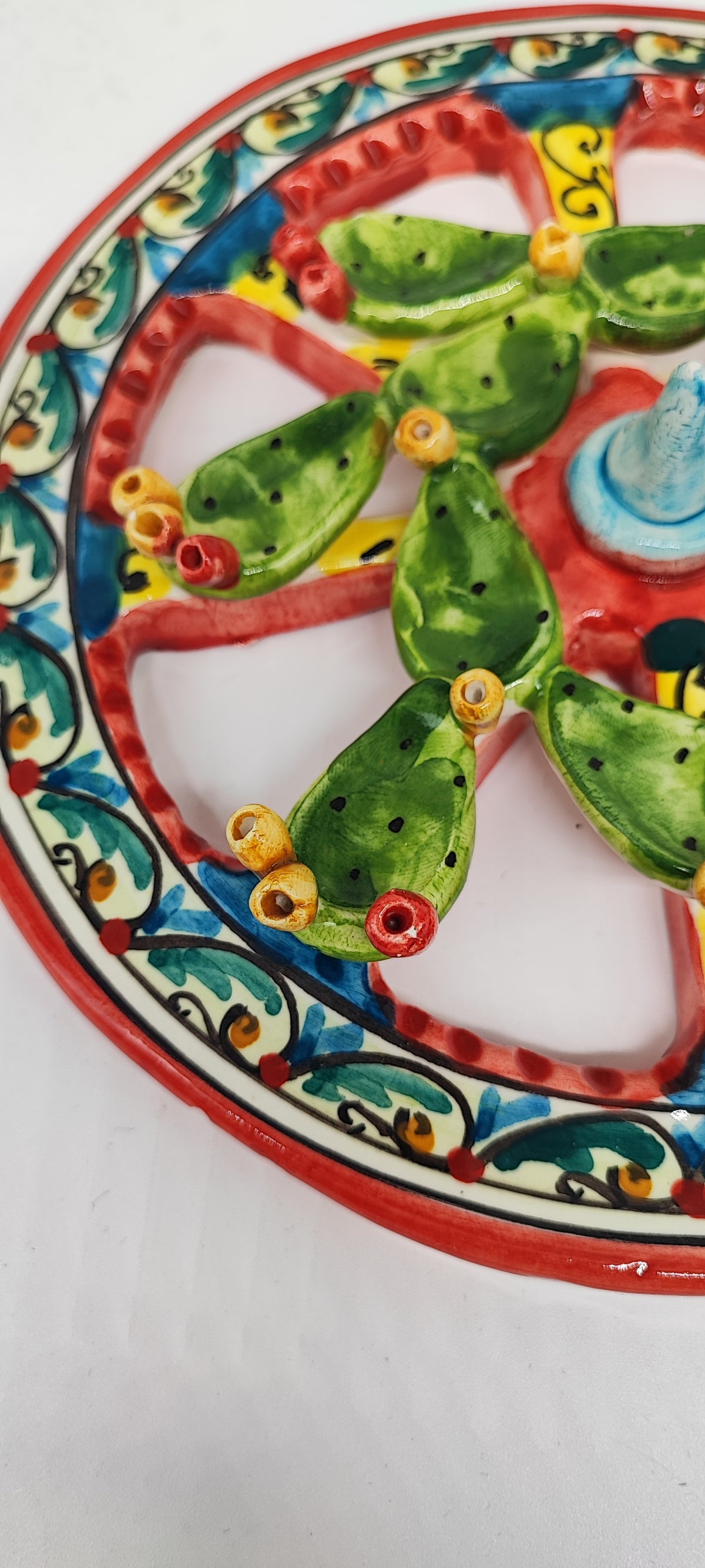 Blue and yellow centre of a ceramic Sicilian cart wheel, surrounded by red spokes and raised green prickly pear pads.
