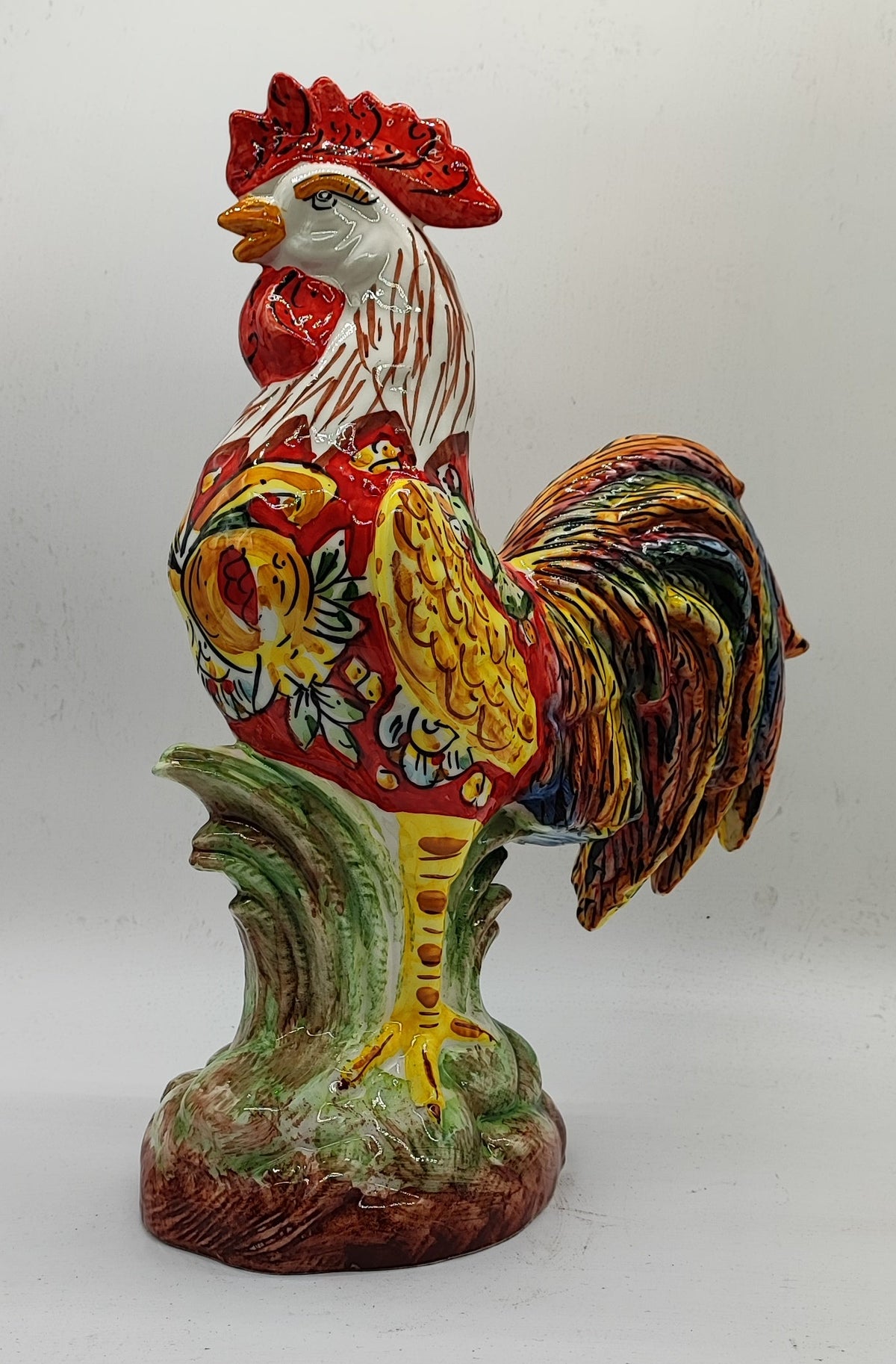 Left-facing view of the ceramic rooster showing its floral decoration, yellow wing and curved multicolored tail.