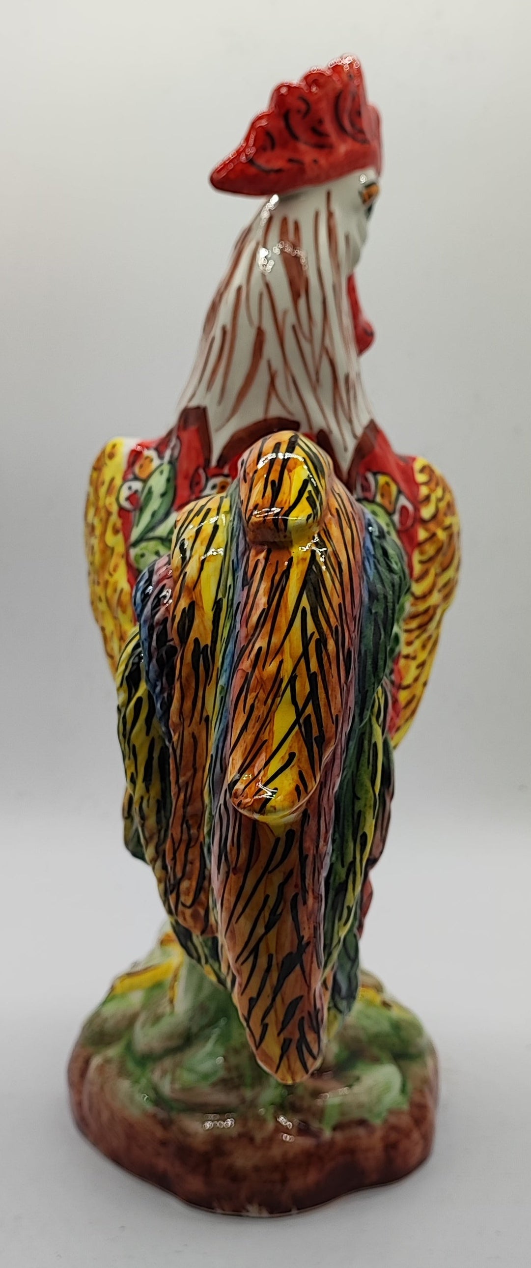 Detail of the ceramic rooster's multicolored tail and sculpted green and brown base.