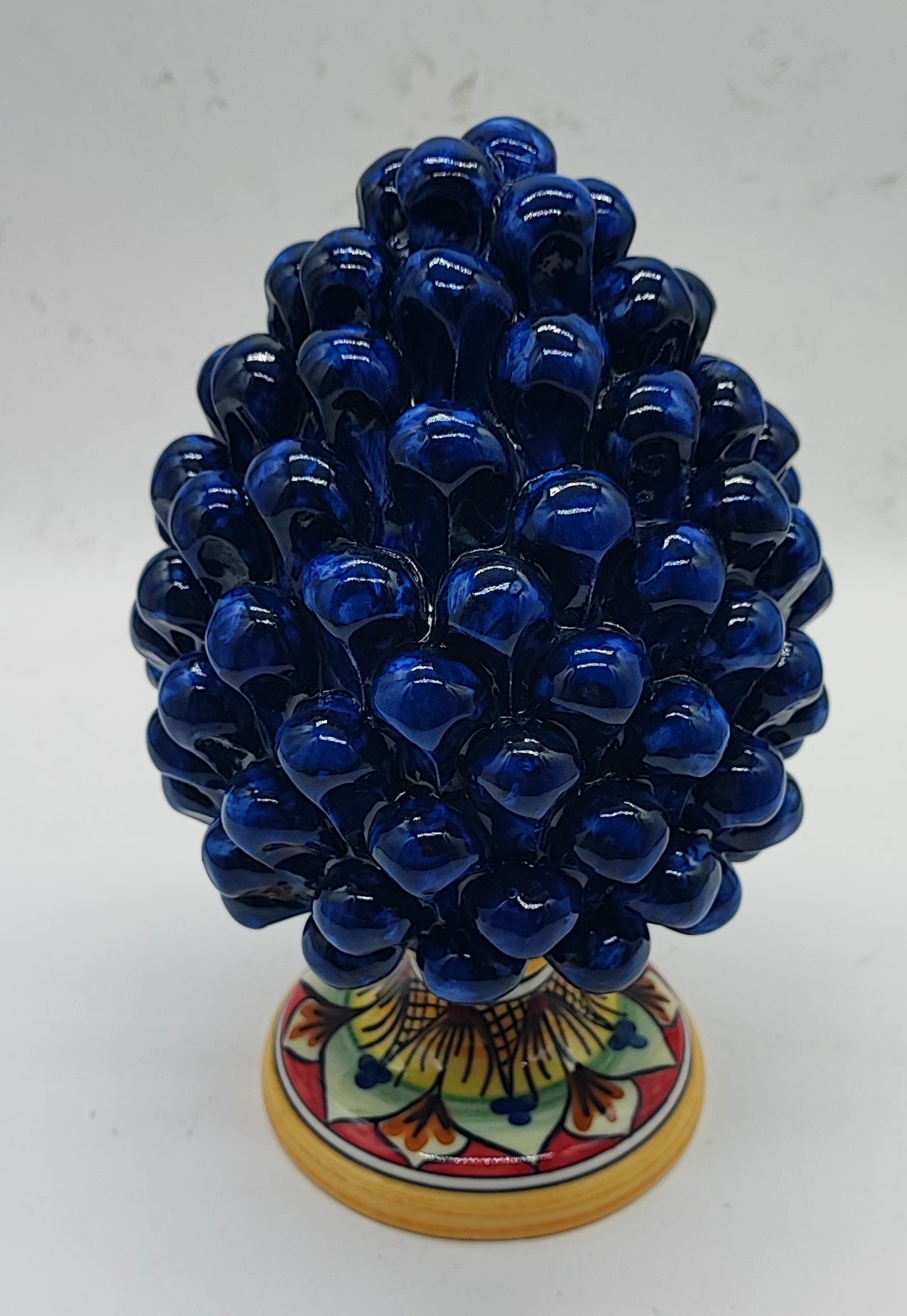 Cobalt blue Sicilian ceramic pine cone on a romantic fireplace mantel with visible fire, height 21 cm
