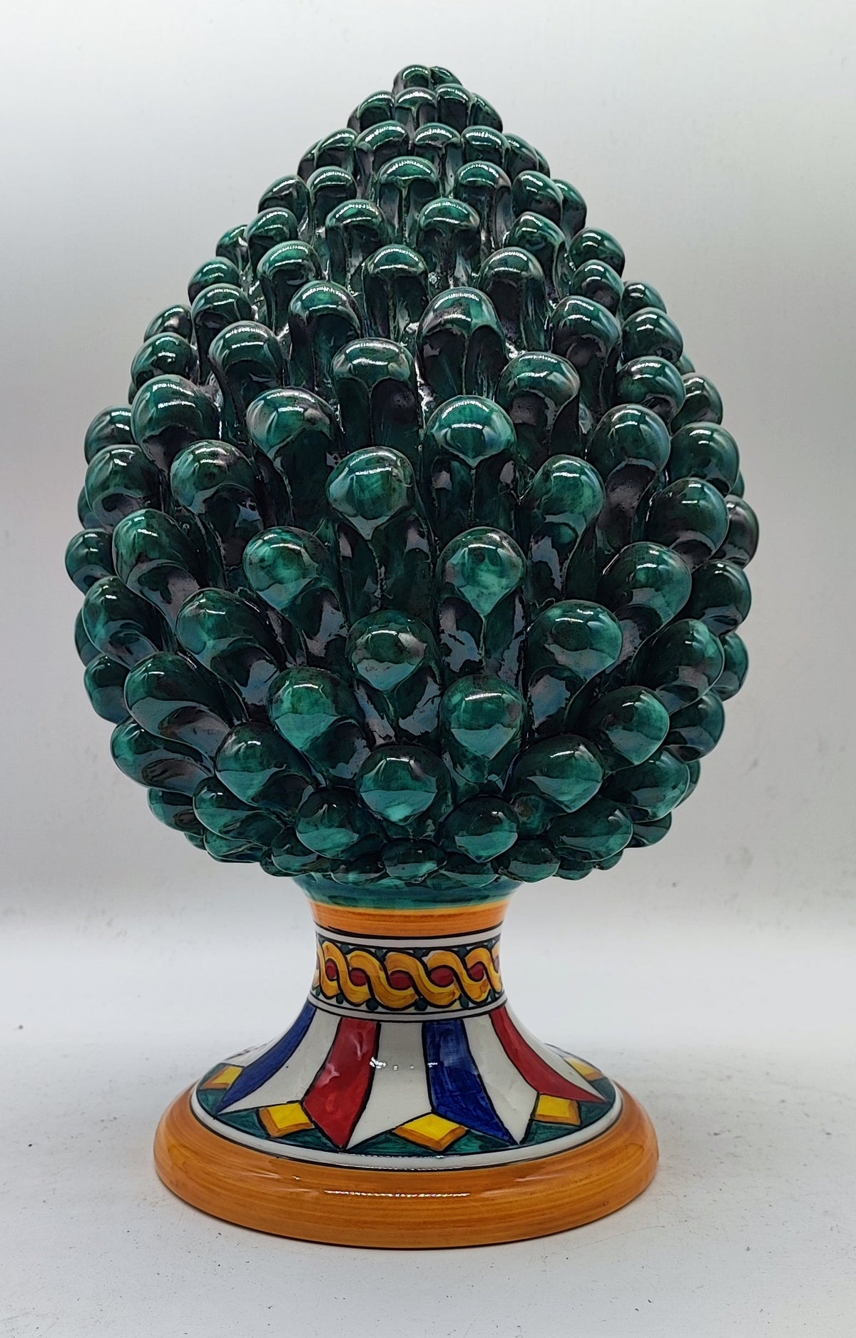 Hand-painted emerald green Sicilian ceramic pine cone styled with festive Christmas greenery and warm holiday decorations.