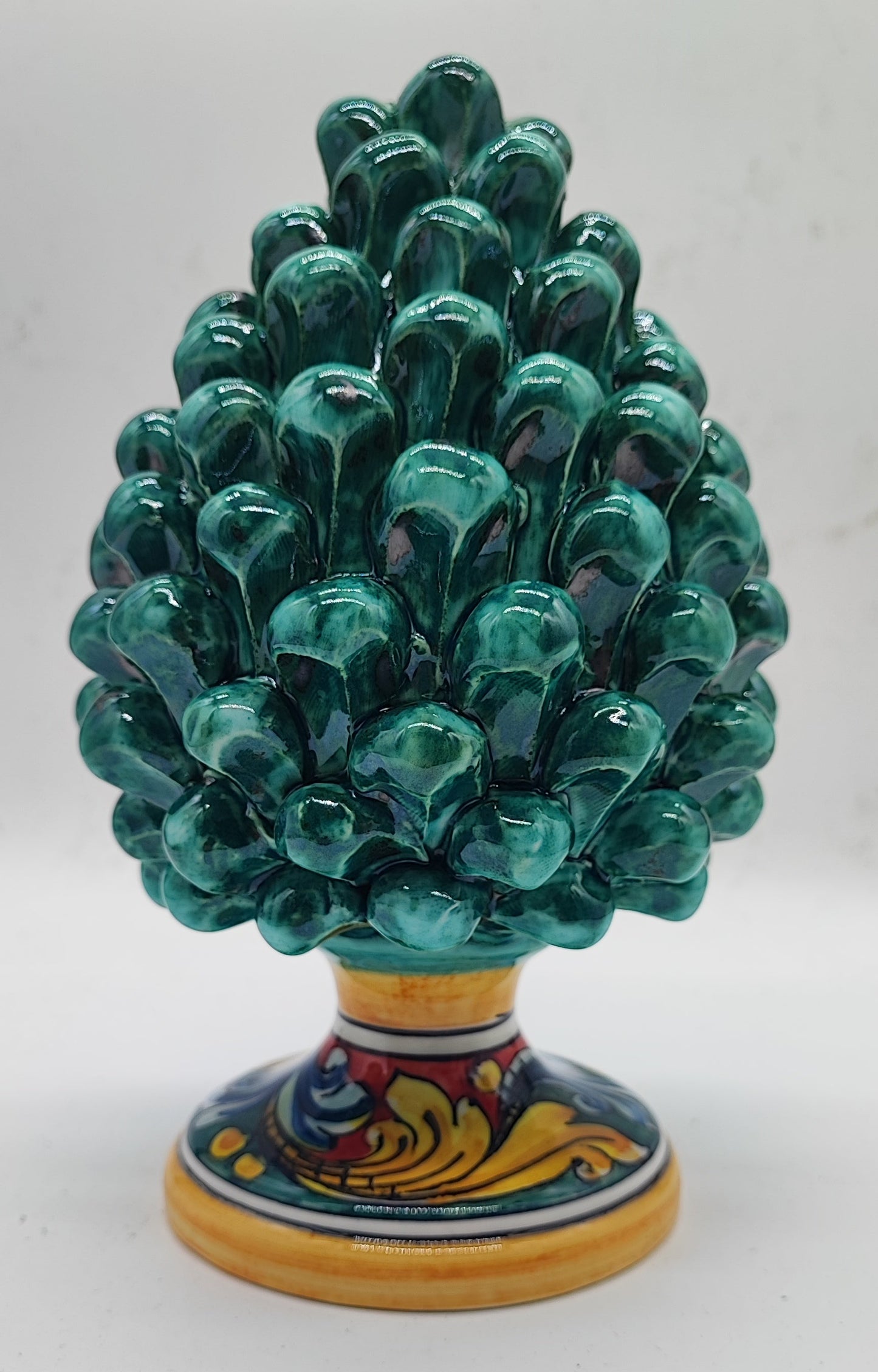 Close-up of an emerald green ceramic pigna with glossy glaze and hand-painted Sicilian scroll decoration