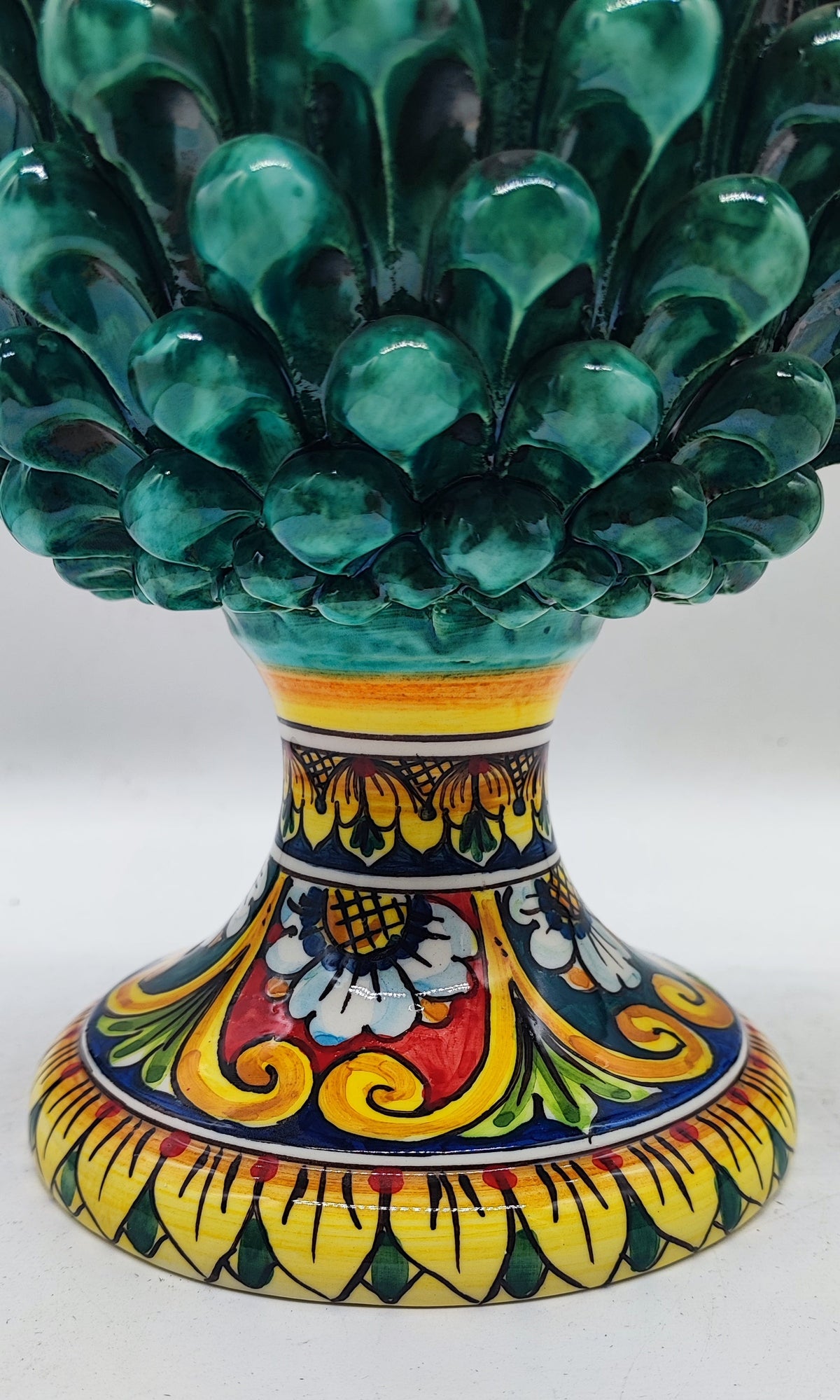 Traditional Caltagirone ceramic pine cone with emerald green glaze and colorful base on an elegant fireplace mantel.
