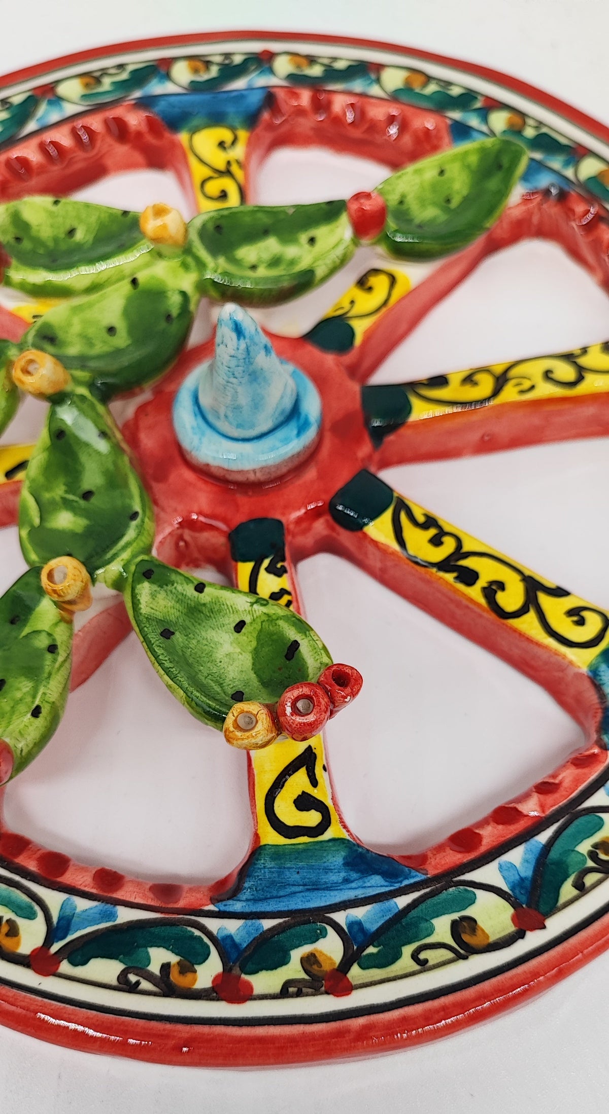 Person holding a colourful ceramic Sicilian cart wheel with raised green prickly pears. Text shows a diameter of 20 cm, 7.9 inches.