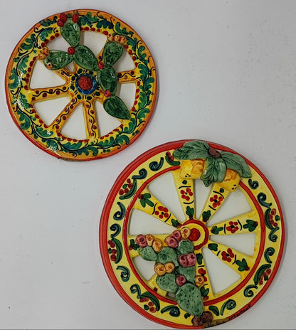 Two yellow Sicilian ceramic cart wheels with raised prickly pear and lemon decorations, held side by side.