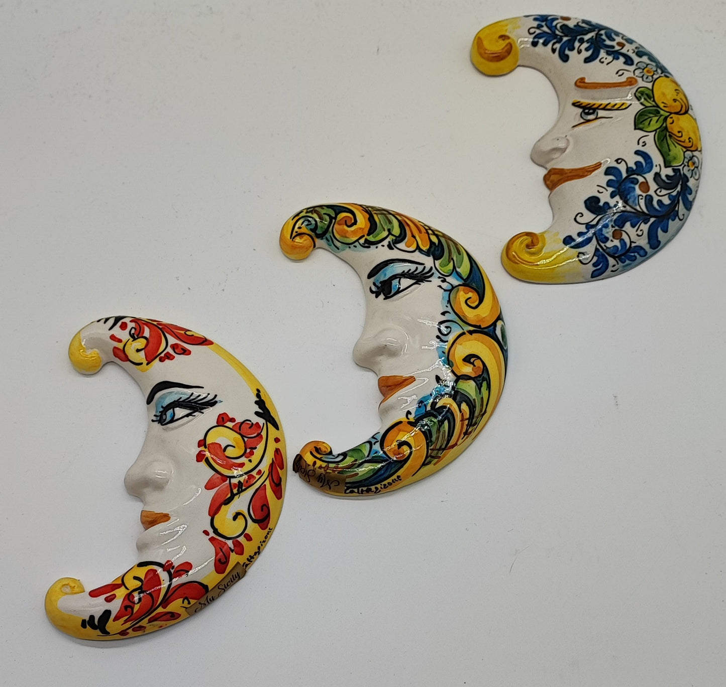 Three handmade Sicilian ceramic moons displayed on an Italian terrace with lemons, oranges and colorful flowers