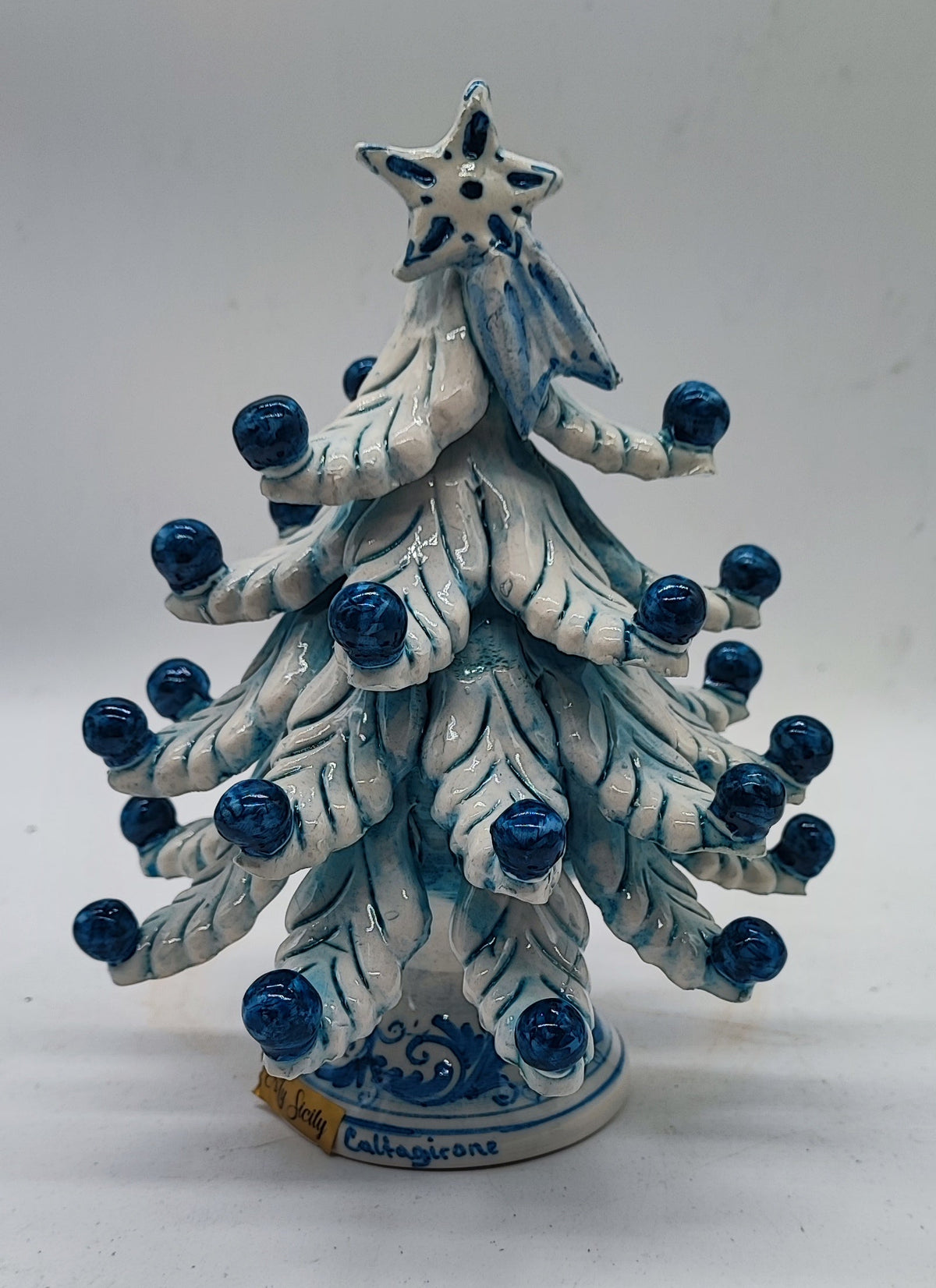 Rear view of a handmade Sicilian ceramic Christmas tree featuring glossy white branches, blue ornaments and decorative ceramic base.