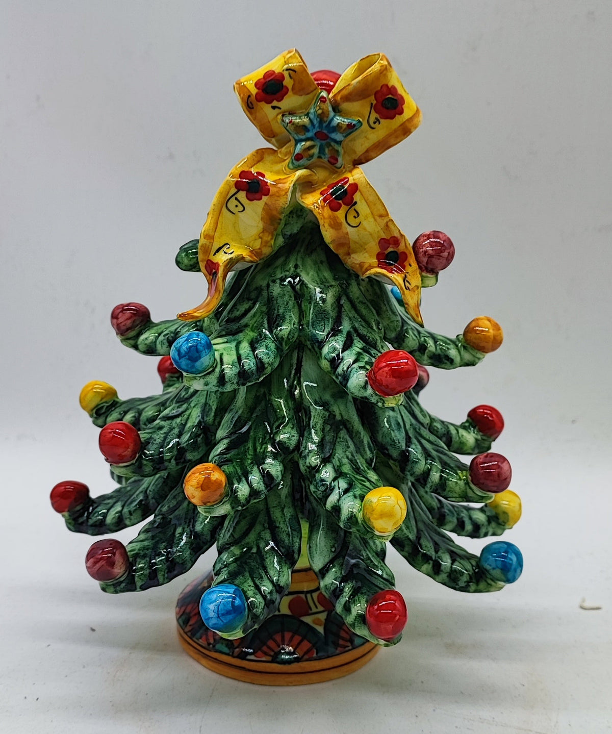 Full front view of a green Sicilian ceramic Christmas tree with multicolored ornaments and floral bow.
