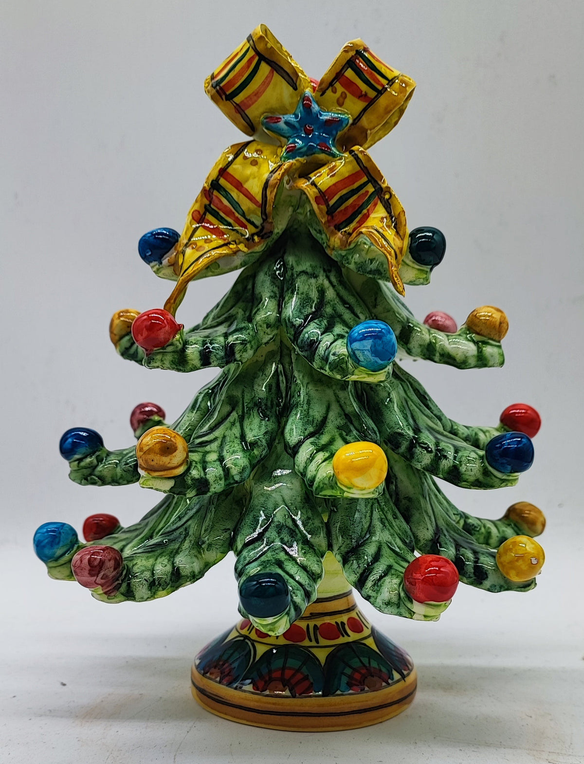 Hand-painted Sicilian ceramic Christmas tree with colorful ornaments and striped yellow bow.