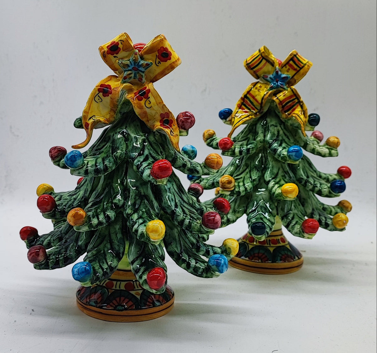 Two traditional Sicilian ceramic Christmas trees showing floral and striped yellow bow designs.