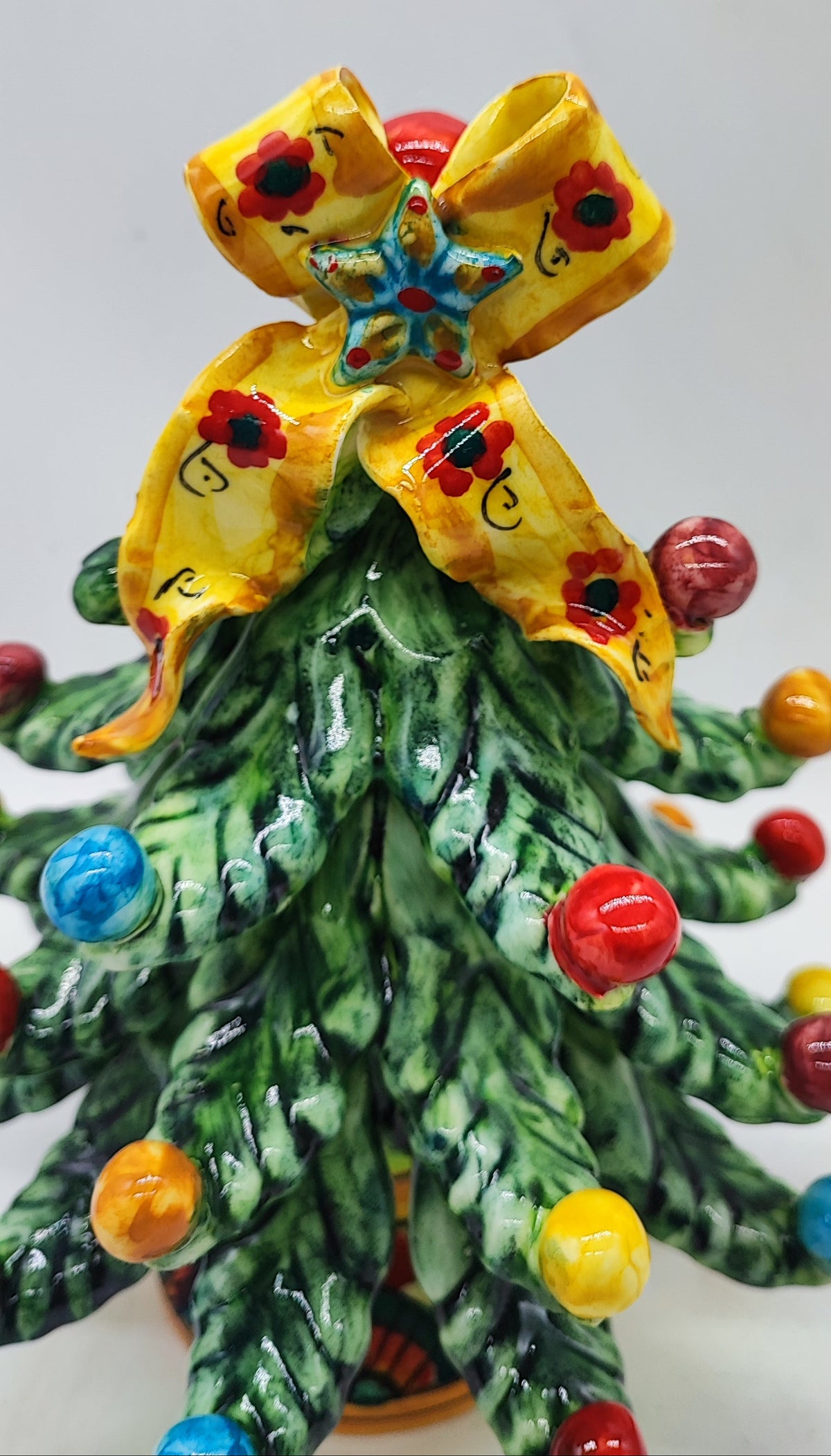Detailed view of the hand-painted yellow floral bow and blue star on a Sicilian ceramic Christmas tree.