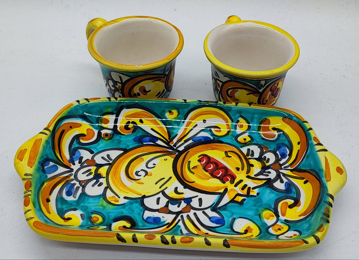 Close-up of a handmade Sicilian ceramic espresso set featuring glossy turquoise glaze, yellow floral patterns and matching colorful coffee cups.