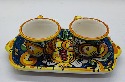 Close-up of a handmade Sicilian ceramic espresso set featuring glossy turquoise glaze, yellow floral patterns and matching colorful coffee cups.