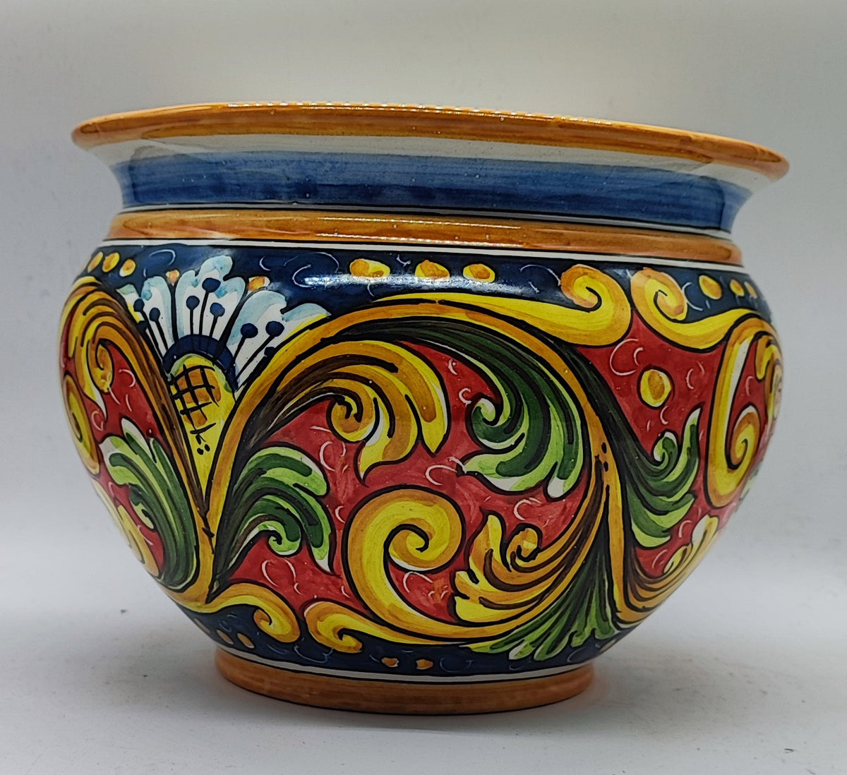 Hand-painted Sicilian ceramic pot displaying a red poinsettia in a warm Christmas home setting.