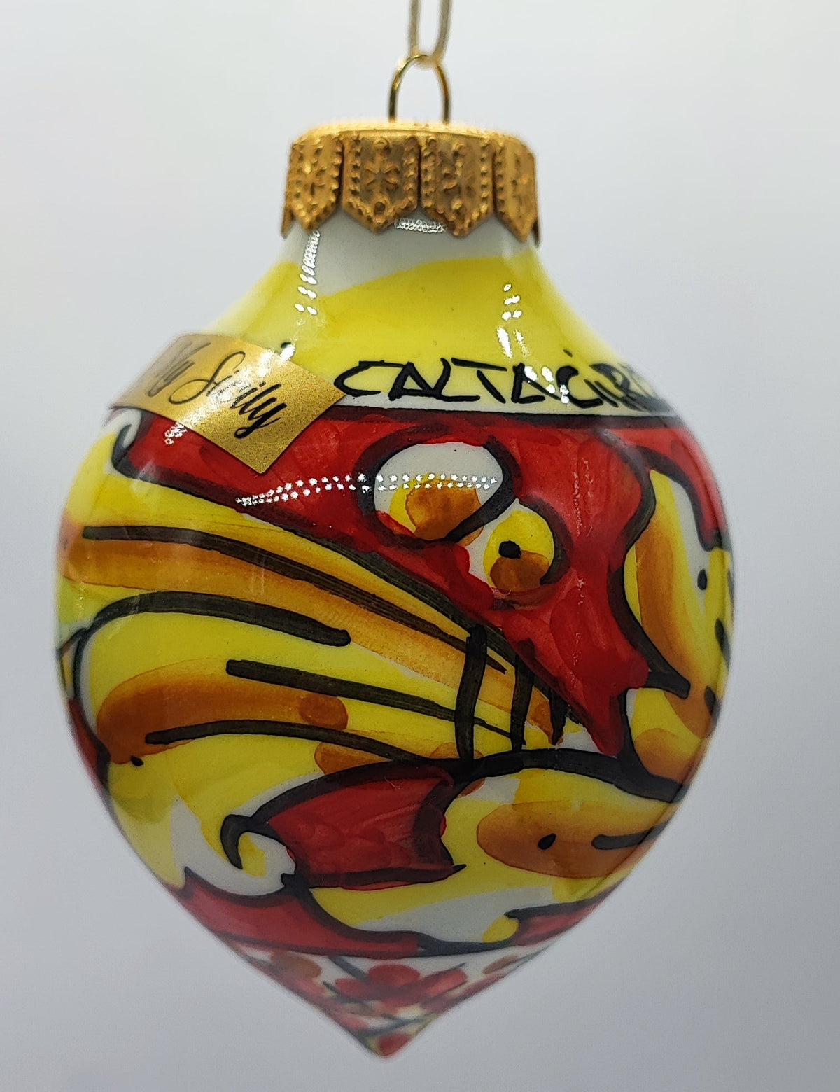 Close-up of a yellow and red hand-painted Caltagirone ceramic Christmas ornament with gold-tone hanging cap.